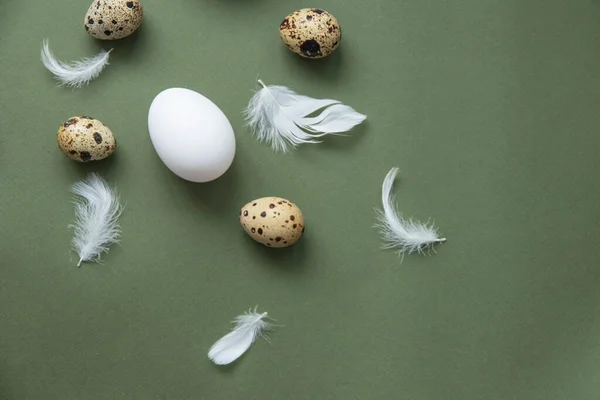 Stylish eggs pattern. Happy Easter. Flat-lay image of eggs and feathers on a green background. Minimalist style.