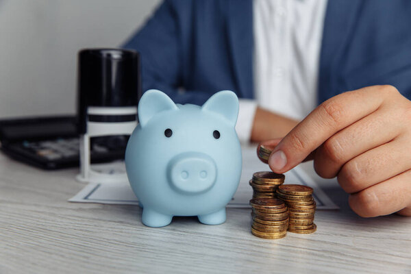 Piggy bank, stamp and mans fingers with coins on desk in office. Save money and management financial concept