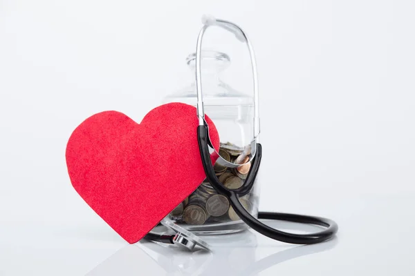 Coins money in glass bottle with stethoscope and red heart close-up. Save money for Medical insurance and Health care concept