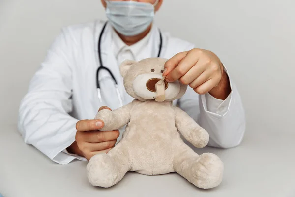 Aardige kinderarts met masker behandelt teddybeer. Concept voor kindergezondheidszorg en -behandeling — Stockfoto