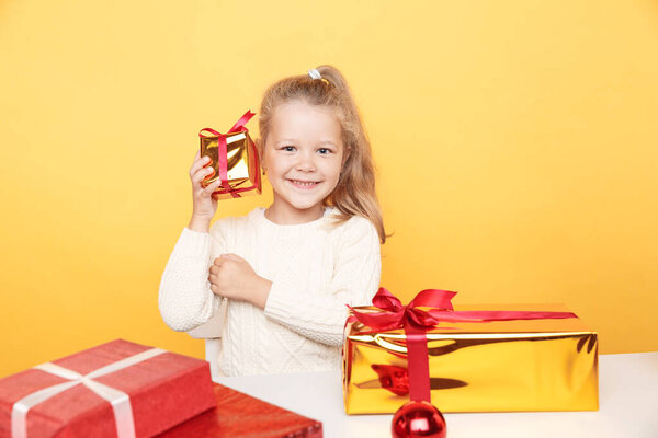 Счастливая девушка в свитере сидит с подарками, изолированными над желтой студией. Концепция Рождества.