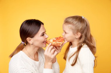 Anne ve kızı birlikte pizza yiyor ve sarı stüdyoda izole bir şekilde eğleniyorlar..