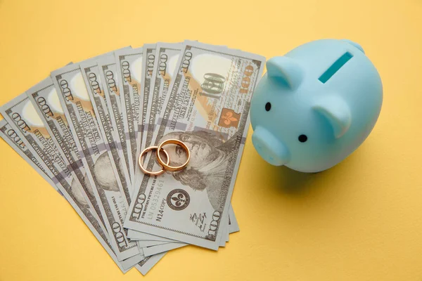 Save money for honeymoon, wedding trip. Piggy bank with rings on money banknotes on yellow background