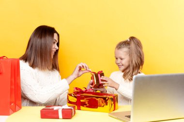 Mutlu anne ve kız Noel hediyeleri ile birlikte sarı arka planda izole bir masada oturuyorlar..