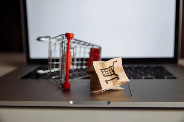Damaged paper box and shopping cart on a keyboard of laptop. Delivery concept. Shipment accident
