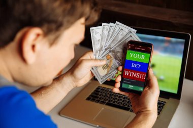 Genç adam en sevdiği takım zaferi için samimi bir mutluluk gösteriyor. Elinde dolar banknotları olan bir adam.