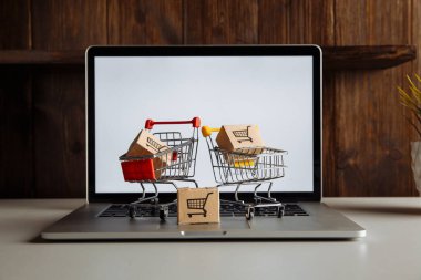 Dizüstü bilgisayarda üç karton kutu ve troller. Çevrimiçi alışveriş, ecommerce ve dağıtım konsepti