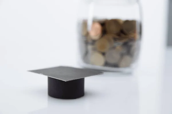 Modelo de graduación sombrero primer plano y monedas en el banco. Ahorro para educación y becas — Foto de Stock