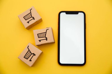 İnternet konsepti üzerinden çevrimiçi alışveriş ve ekommerce: sarı arka planda kutular ve akıllı telefon