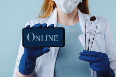 Diş kliniğinde poz veren güzel bir kadın dişçinin portresi. Elinde yeşil ekranlı akıllı telefon var ve kameraya mobil uygulama veya web sitesi sunuyor.