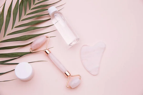 Rose quartz jade roller and gouache scraper on pink background. Anti age, lifting and beauty care at home