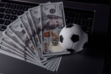 Futbol topu ve dolar banknotları yakın plan klavyede. Spor, kumar, bahis konsepti
