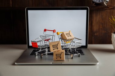 Dizüstü bilgisayarda karton kutular ve troller. Çevrimiçi alışveriş, ecommerce ve dağıtım konsepti