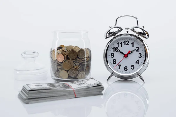 Bank with coins, dollar banknotes and alarm clock. Time is money concept