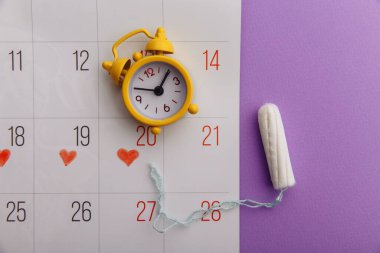 Takvim, pamuk tampon ve leylak arka planda sarı alarm saati. Dişilerin adet döngüsü kavramı
