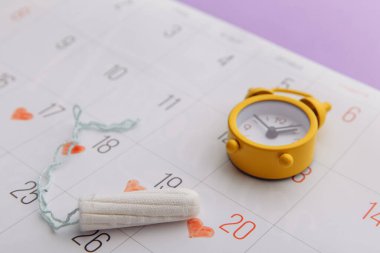 Takvim, pamuk tampon ve leylak arka planda sarı alarm saati