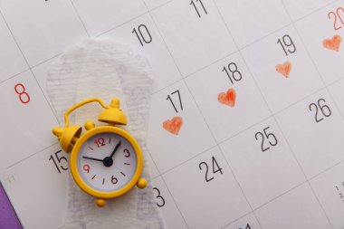 Takvim, adet pedleri ve sarı alarm saati yakın plan.