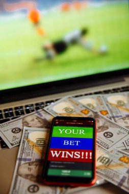 Dolar banknotları üzerinde kumar mobil uygulamalı akıllı telefon ve çevrimiçi futbol maçı yayınlı laptop.