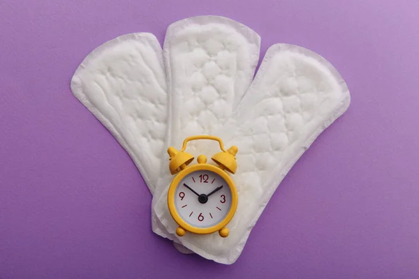 バックライラック上の精神パッドと黄色の目覚まし時計。女性の月経周期の概念 — ストック写真