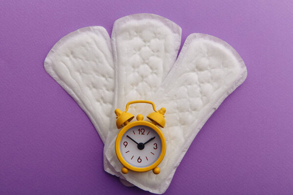 Females menstrual cycle concept. Sanitary pads with yellow alarm clock