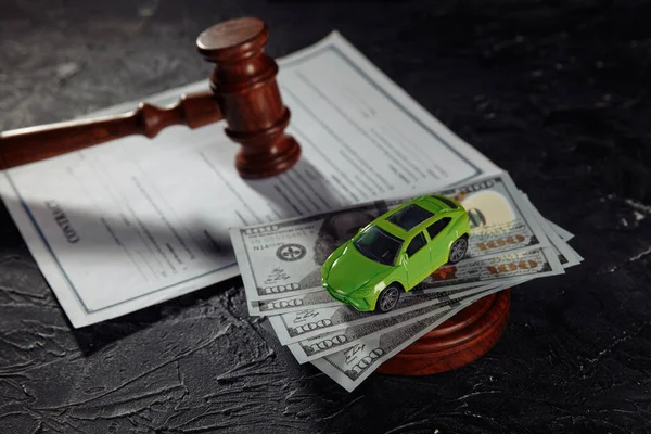 Toy car on dollar banknotes and wooden judge gavel with contract