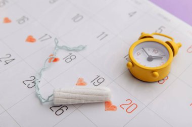 Takvim, pamuk tampon ve leylak arka planda sarı alarm saati.