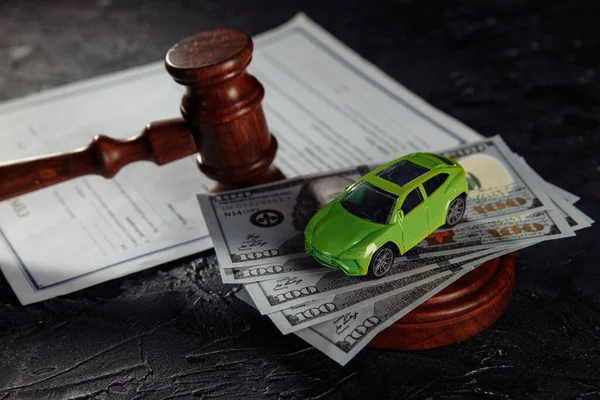Toy car on dollar banknotes and wooden judge gavel with contract close-up