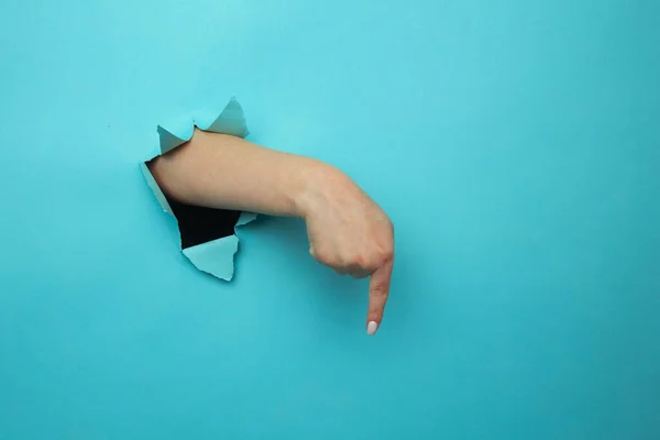 Finger pointing down through torn blue paper wall. Hand gestures of direction — Stock Photo, Image