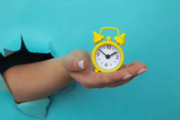 A mão da mulher segura o despertador amarelo através de um buraco de papel. Conceito de gestão do tempo e prazo — Fotografia de Stock