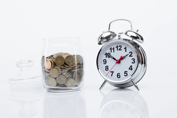 Banco con monedas y despertador en una mesa de cristal. El tiempo es concepto de dinero — Foto de Stock