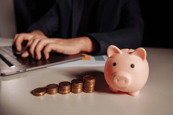 Stos monet i różowa świnka przy biurku. Koncepcja oszczędzania pieniędzy — Zdjęcie stockowe