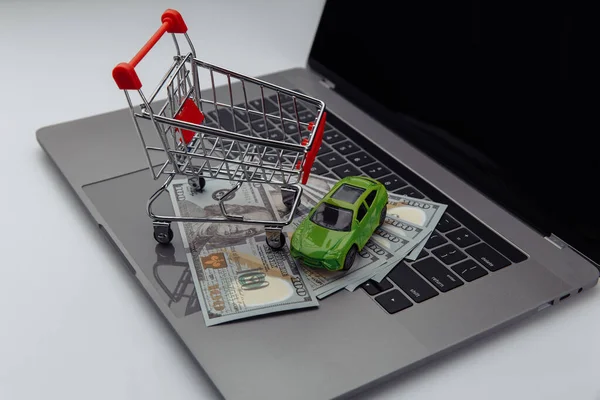 Green car with dollar banknotes and shopping cart on keyboard. Online purchase car concept