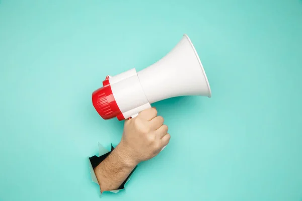 Male hand arm hold megaphone isolated through torn blue background — Stock Photo, Image