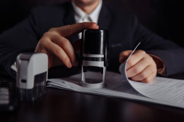 İşadamı kâr sözleşmesini onaylıyor. Para yığını, kontrat ve pullar masanın üstünde.