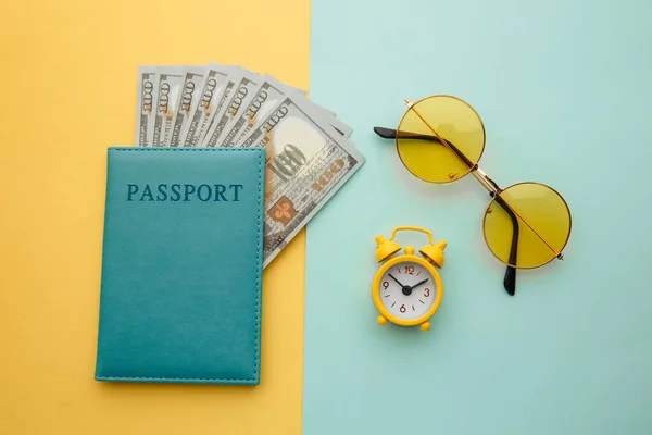 Hora da viagem. Relógio despertador, óculos de sol e passaporte com notas de dinheiro em fundo colorido — Fotografia de Stock
