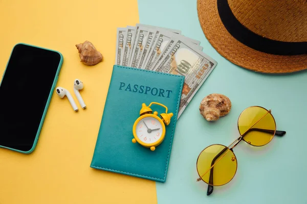 Concetto turistico. Occhiali da sole, smartphone, cappello e passaporto con banconote da soldi su sfondo giallo blu — Foto Stock