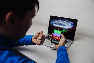 Erkek taraftar dizüstü bilgisayarında futbol maçı seyrediyor, favori takım için tezahürat yapıyor ve bahisçilerin web sitesinde bahis oynuyor.