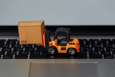 Turuncu forklift modeli ve klavyede karton kutu. Kurye hizmeti kavramı