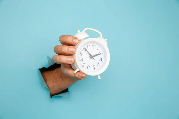 La mano sostiene el despertador a través de un agujero de papel. Gestión del tiempo y concepto de plazo —  Fotos de Stock