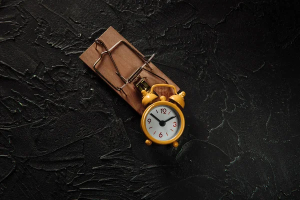 Reloj despertador amarillo en una ratonera sobre un fondo gris, concepto de trampa de tiempo —  Fotos de Stock