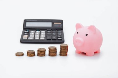 Finans Tasarruf, gelecek yatırımlar ve acil durum kullanımı için tasarruf. Beyaz arka planda pembe bir kumbara, bozuk para kulesi ve hesap makinesi.