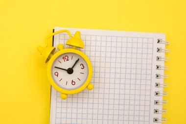 Sarı zemin üzerinde sarı alarm saati ve defter, metin için boş alan