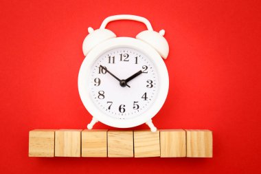 Metin için yeri olan yedi tahta küp ve kırmızı zemin üzerinde beyaz alarm saati. Zaman para konseptidir. Süre kısıtlı. İş için son gün. Boşluğu kopyala