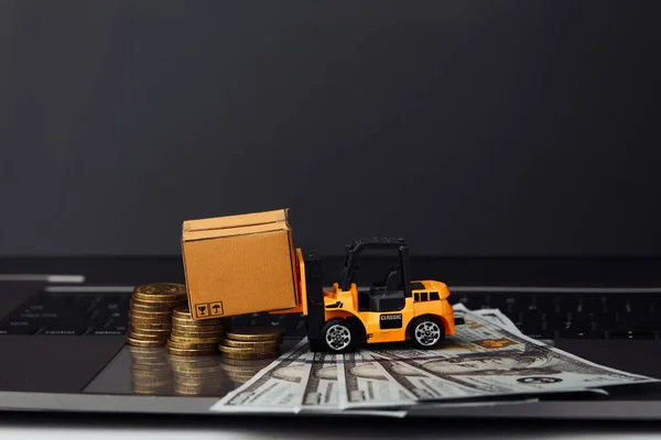 Mini model of forklift with boxes and money on keyboard. Logistics and delivery concept