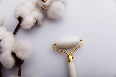 Doğal kaldırma için yüz masajı. Beyaz arka planda taş rulo ve pamuktan bir dal