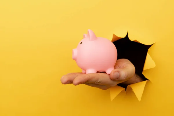 黄色の紙の穴を通ってピンクの貯金箱で手。財務・経営の考え方 — ストック写真