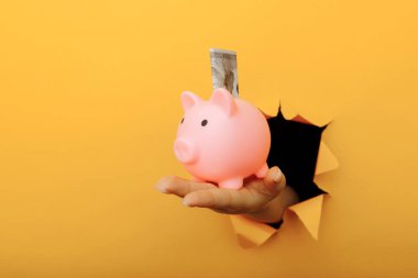 Elinde domuz kumbarası ve sarı bir kağıt delikten geçen bir dolar banknotuyla. Yatırım ve tasarruf