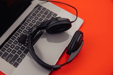 Kırmızı arka planda dizüstü bilgisayar ve kulaklık. Teknoloji konsepti