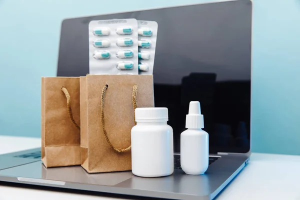 Koncepcja zakupów medycznych online. Torby papierowe z lekami i pigułkami oraz konkursy na laptopie na niebieskim tle — Zdjęcie stockowe