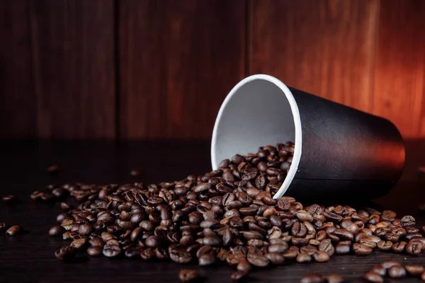 Una taza de papel de café con granos de café sobre fondo de madera — Foto de Stock